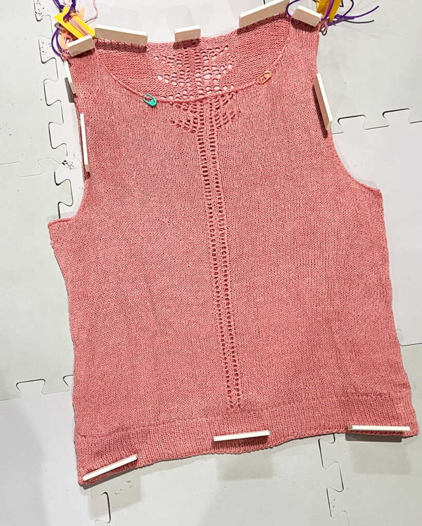 Pink hand-knitted top, blocking a lace knit tank top or vest, featuring detailed yarn work and vertical stitch pattern