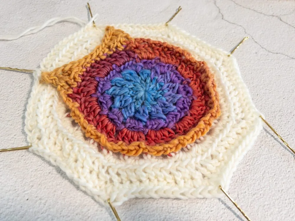 Close-up of a colorful crocheted owl motif pinned flat with bobby pins, showing a missing ridge on the front edge where the last row was not worked into the back loop only.