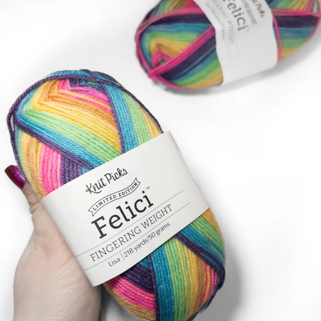 Two skeins of Knit Picks Felici fingering weight yarn in the Lisa colorway, with the label visible on one skein. The yarn is striped in bright colors including teal, green, yellow, orange, pink, purple, and navy.