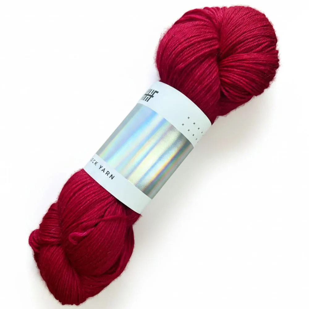 A skein of deep red Hedgehog Fibres sock yarn with a holographic label, ideal for knitting and crafting projects. Color: Merlot.