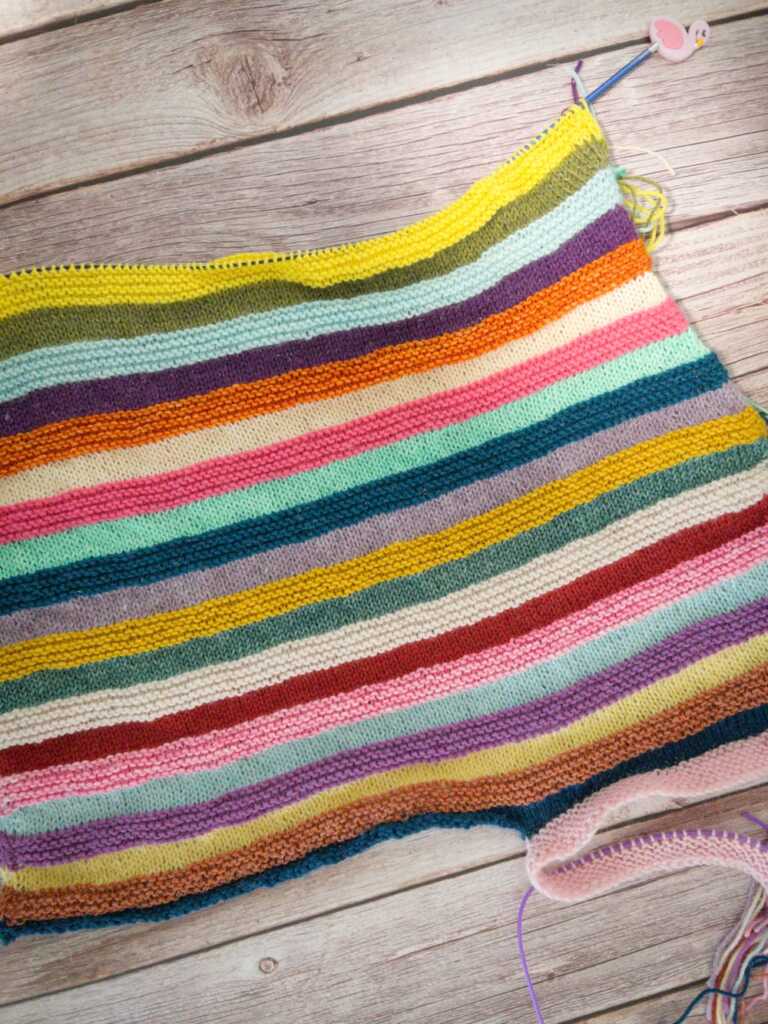 Handmade knitting project with colorful striped yarn in garter stitch. Pattern is Mix Tape Tee by Wool and Pine.