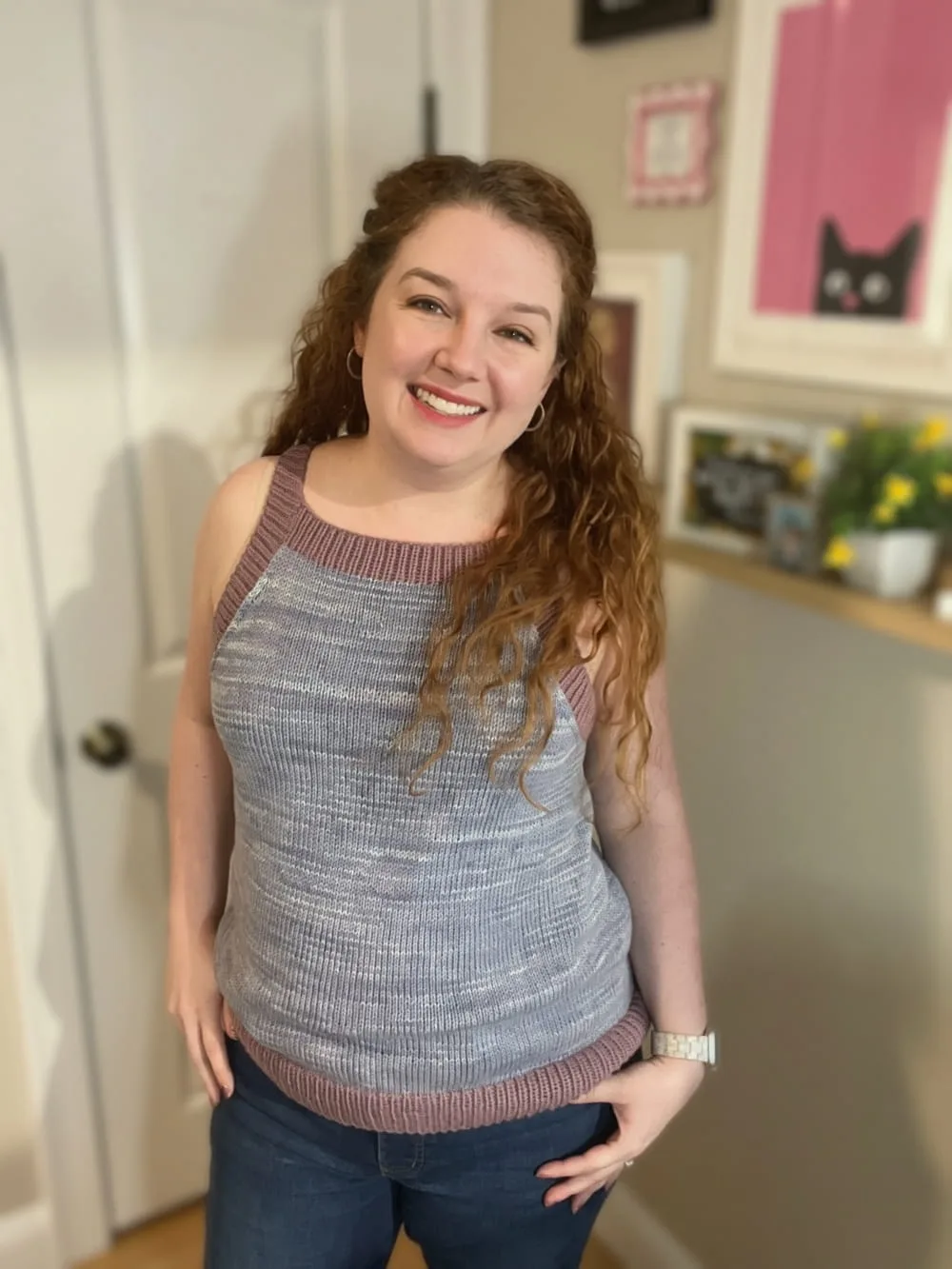Smiling woman models a handmade knitted tank top with blue-grey tonal yarn and mauve ribbed trim. Pattern is Grasslands Tank and the yarn is dyed with natural indigo.