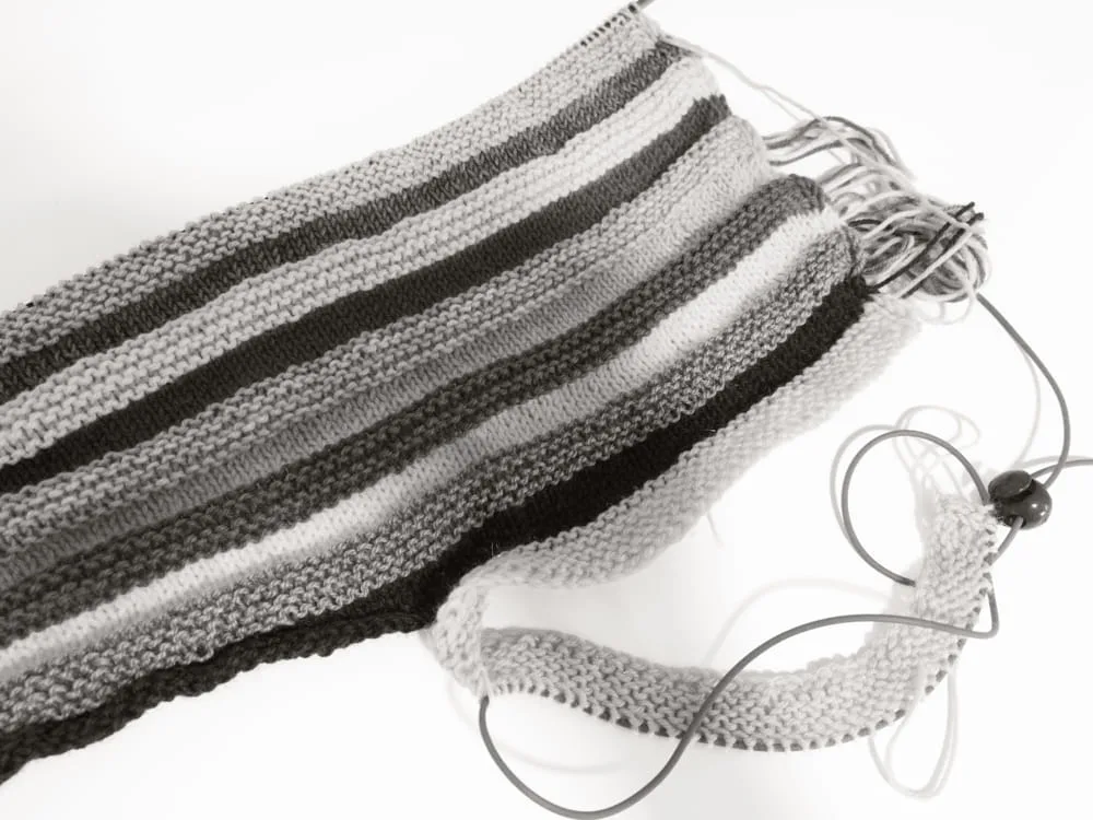 Striped knitting project in garter stitch using various yarn shades on circular needles