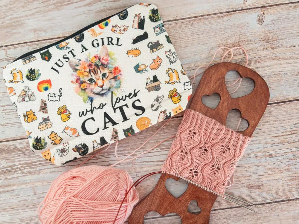 Pink lace knitting project on a wooden yarn winder with a ball of yarn and a 'Just a girl who loves cats' pouch