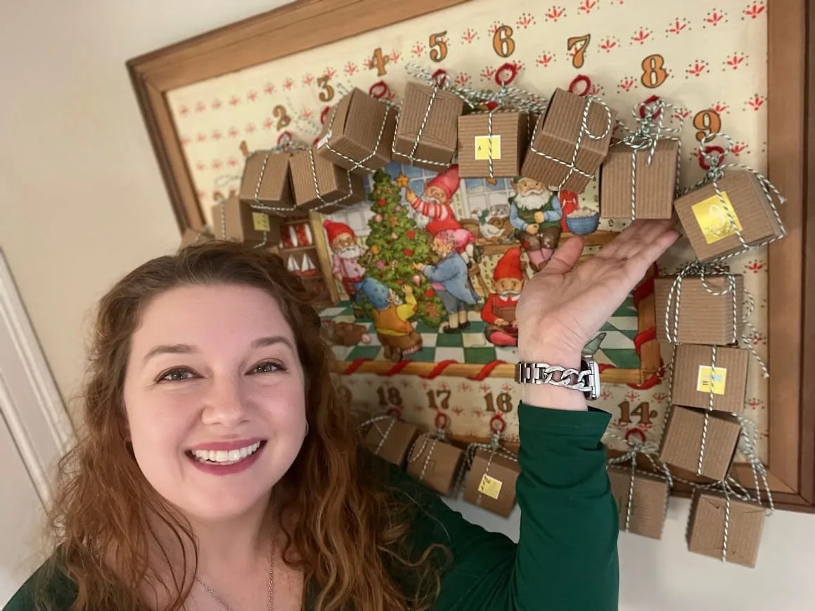 Smiling knitter showing a homemade knitting advent calendar with numbered gift boxes, perfect for daily knitting or yarn surprises