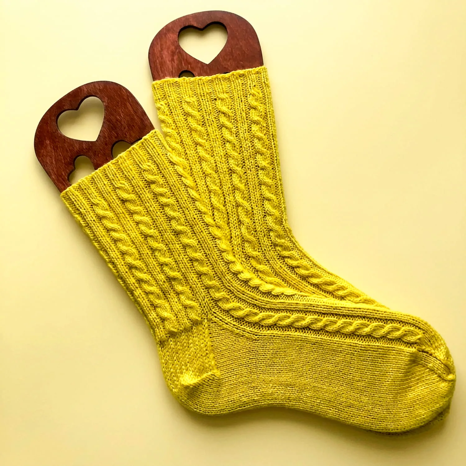 Hand-knitted yellow cable knit socks displayed on wooden heart sock blockers