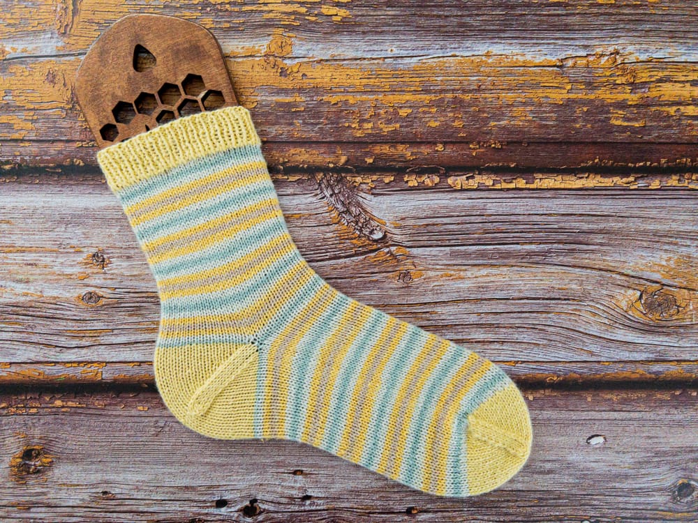 Vibrant hand-knitted striped sock in yellow and blue yarn, displayed on a wooden sock blocker