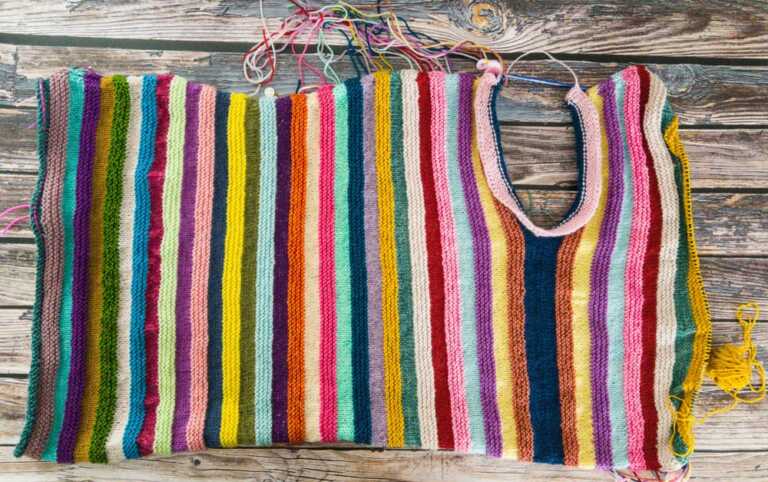 Colorful striped knitting project in progress with a U-shaped neckline, showcasing vibrant yarn colors for unique handmade knitwear