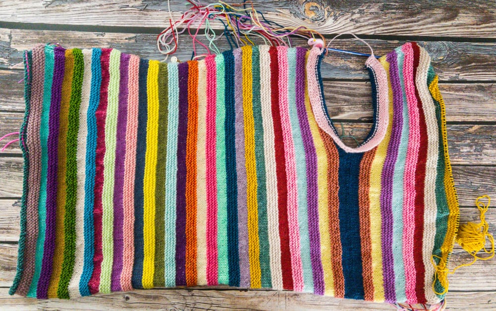 Colorful striped knitting project in progress with a U-shaped neckline, showcasing vibrant yarn colors for unique handmade knitwear