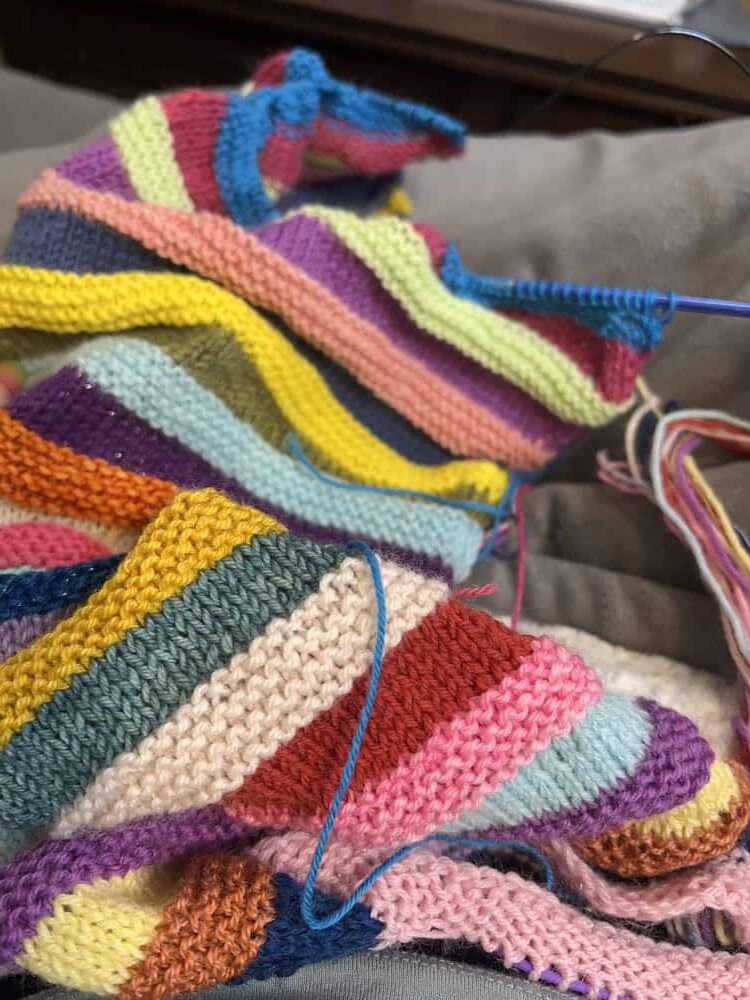 Vibrant knitting project with colorful yarn stripes in garter stitch on a circular needle. Mix Tape Tee by Wool and Pine.