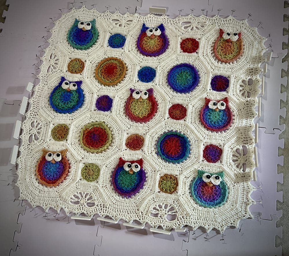 Colorful crocheted owl blanket, a handmade yarn art project, featuring vibrant motifs, being blocked